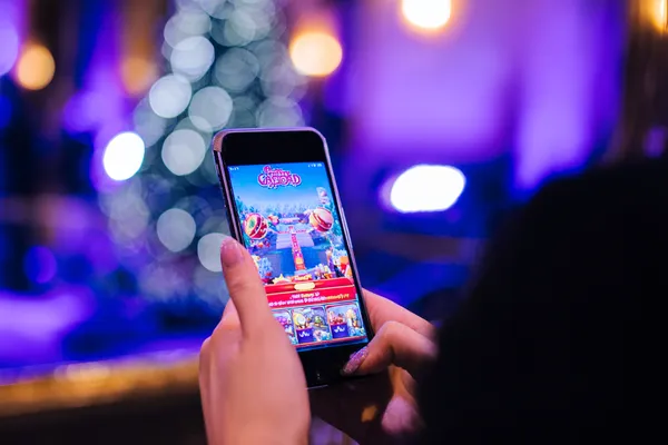 একজন তরুণী তার ফোনে আরাম করে গেম খেলছেন, আর চারপাশে ভাসছে ডায়নামিক ক্যাসিনো উপাদান—যা 4777BIT অ্যাপের মসৃণ মোবাইল অভিজ্ঞতাকে ফুটিয়ে তোলে।